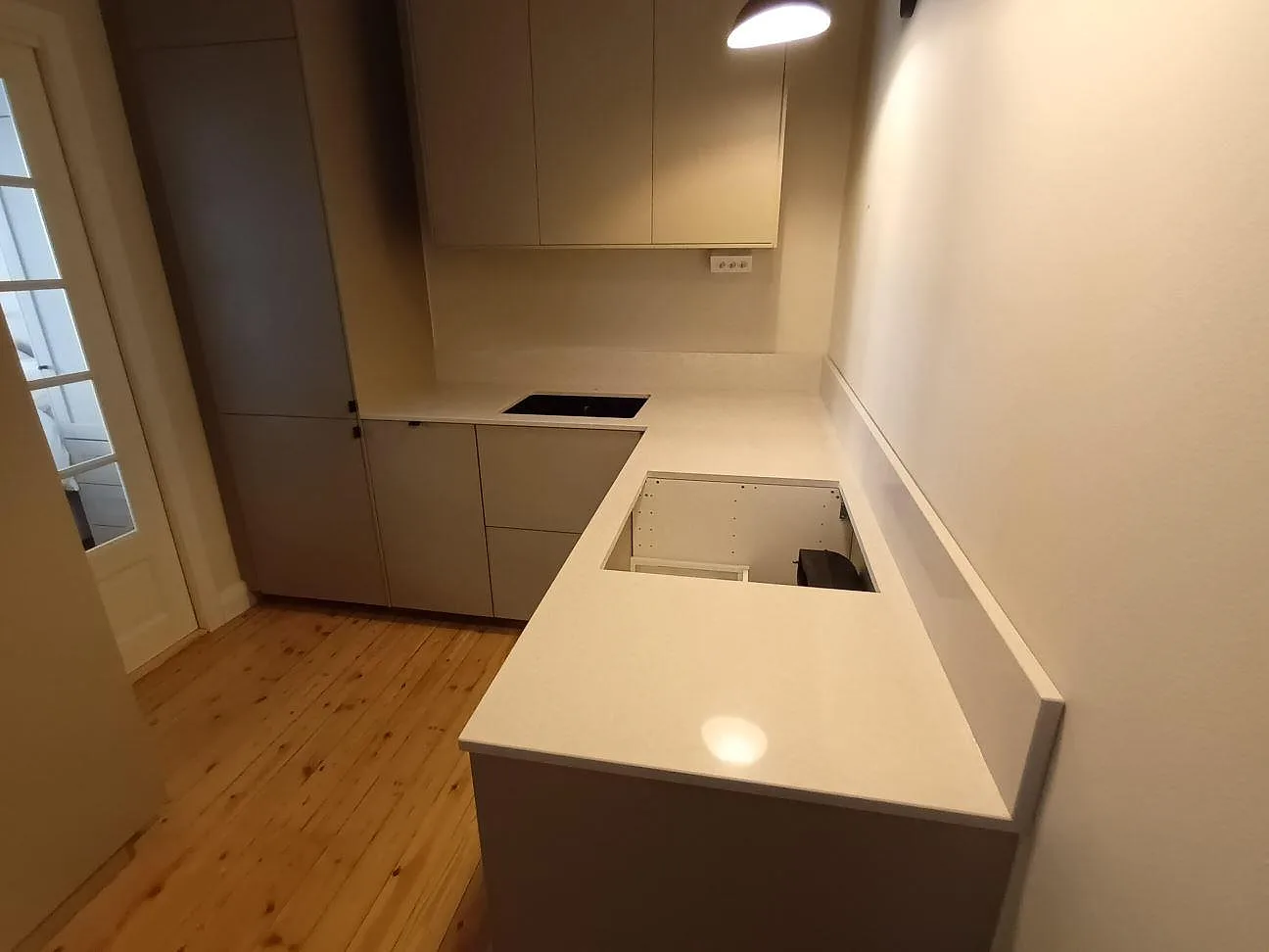Köksbänkskiva i vit Caesarstone Alpine Mist, polerad, i ett vinkelkök i Stockholm med underlimmad mörk komposithoar och urtag för häll under montering.