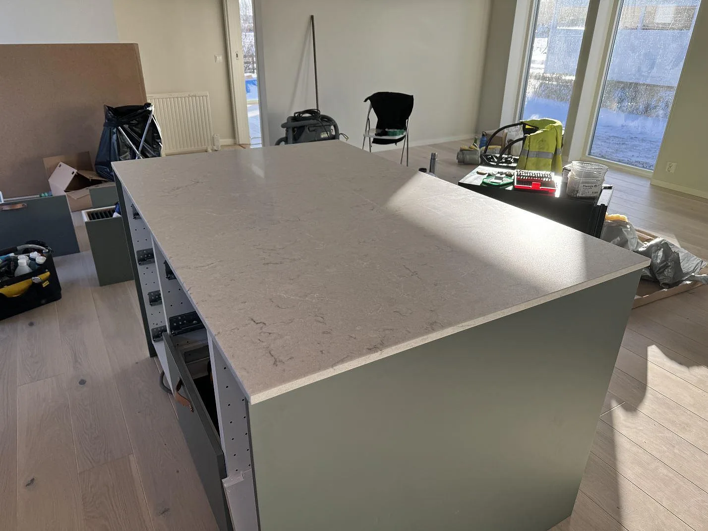 Närbild på köksö i polerad Caesarstone Bianco Drift med ljusgrå ådring och montering pågående i Åsa.