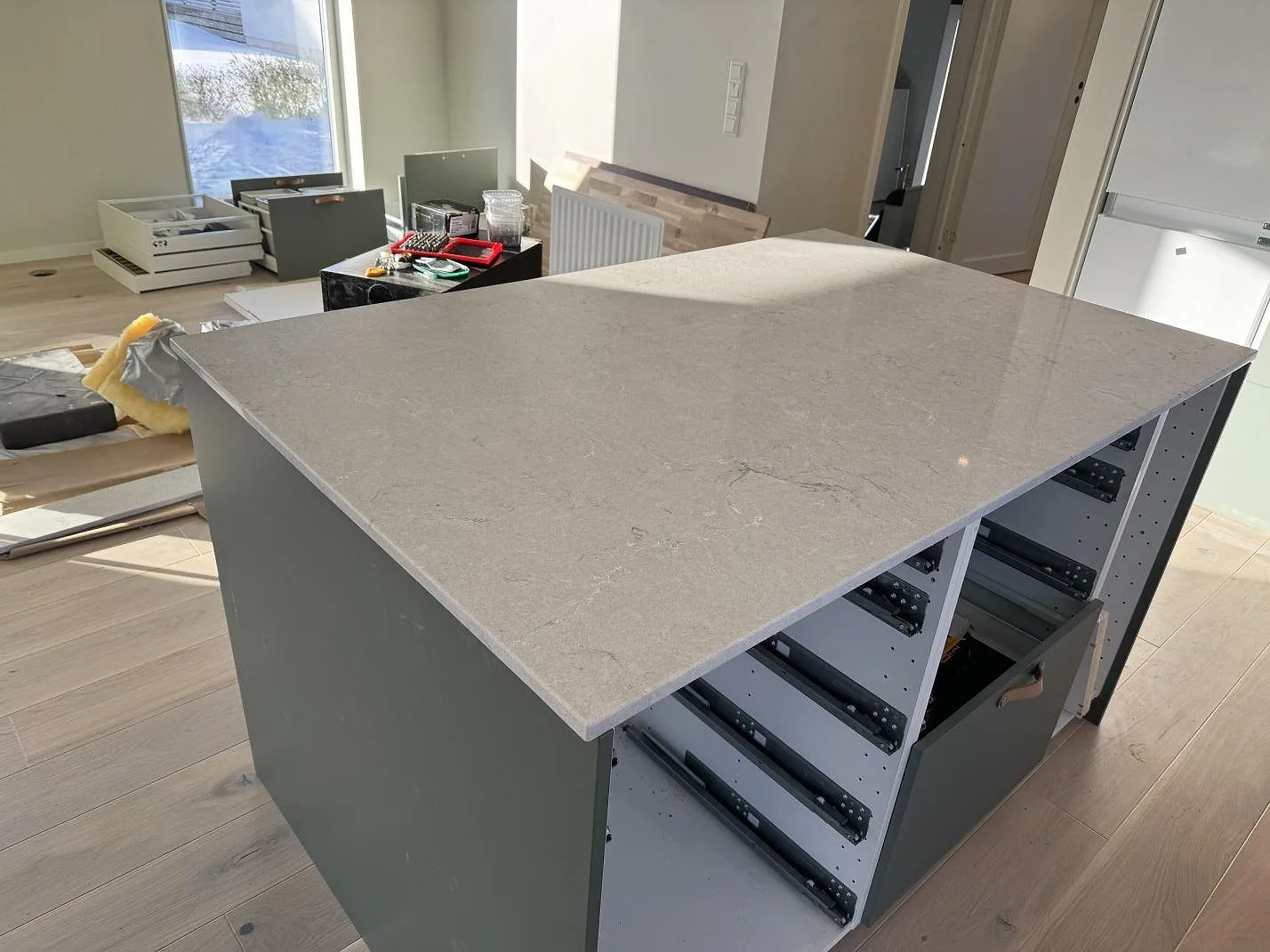 Stor köksö med polerad Caesarstone Bianco Drift i ljusgrå komposit på grågröna köksstommar i Åsa.