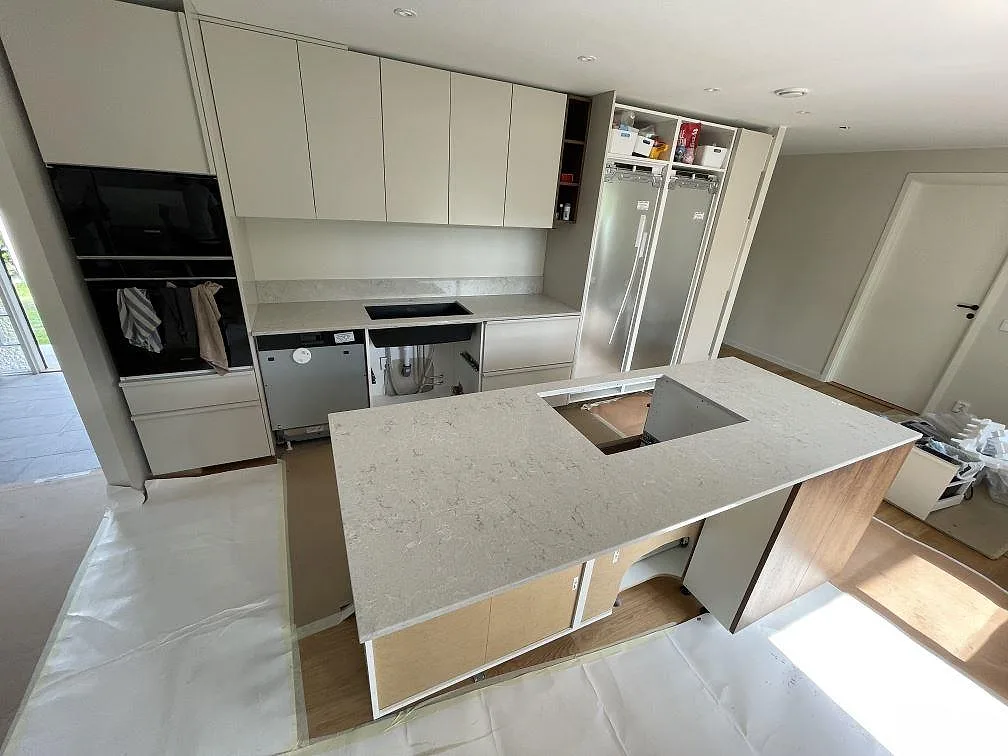 Köksbänkskiva och köksö i Caesarstone Bianco Drift, polerad vit kvartskomposit med grå ådring, under montering i ett kök i Ekerö.
