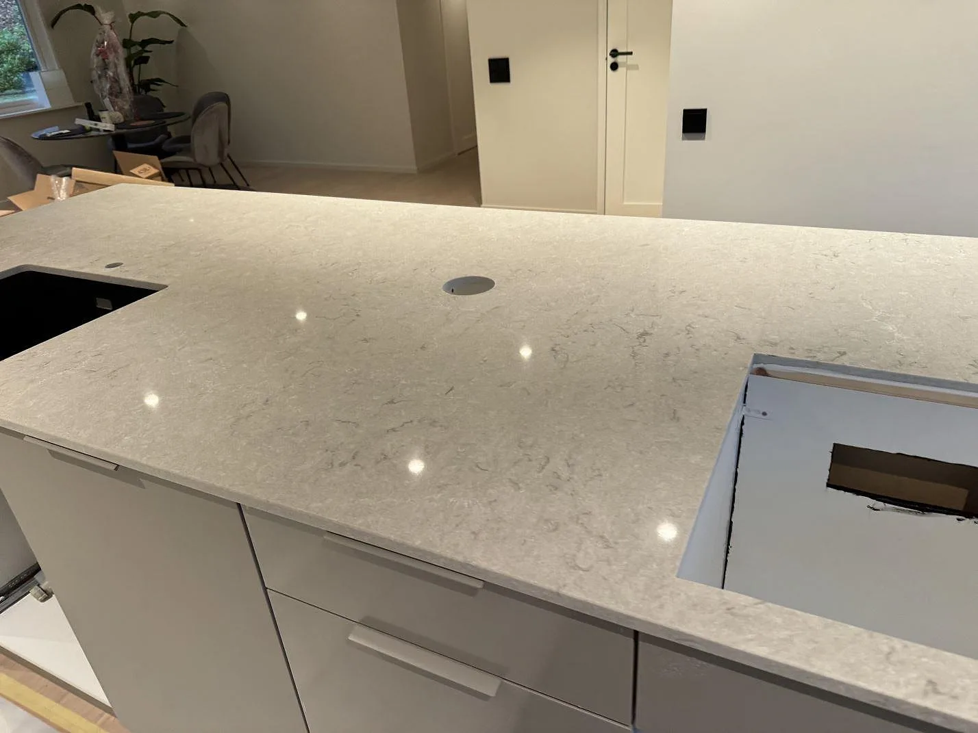 Polerad Caesarstone Bianco Drift köksbänkskiva med blandarhål, svart diskho och hällöppning under montering i Halmstad.