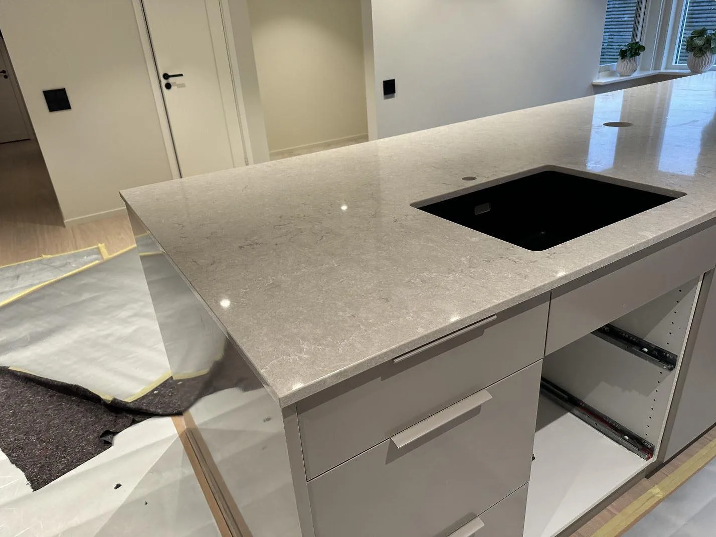 Köksbänkskiva i Caesarstone Bianco Drift, polerad kvartskomposit, med svart diskho monterad under stenen i Halmstad.