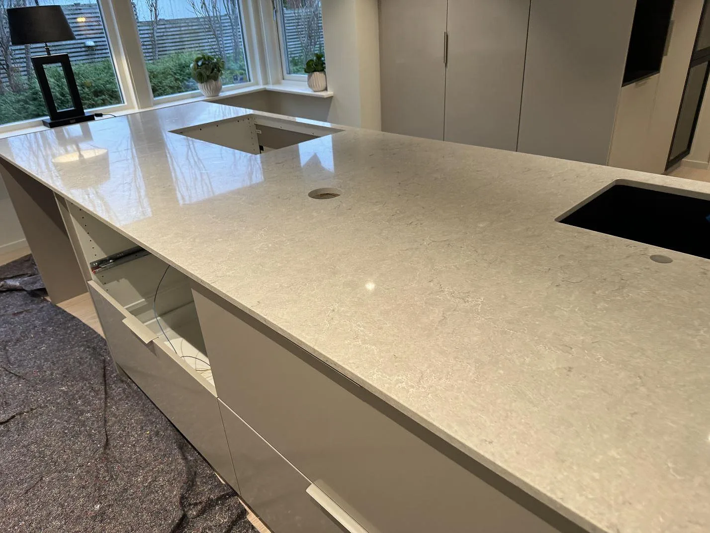 Ljus polerad Caesarstone Bianco Drift som köksbänkskiva med synlig hällöppning, blandarhål och svart diskho i Halmstad.
