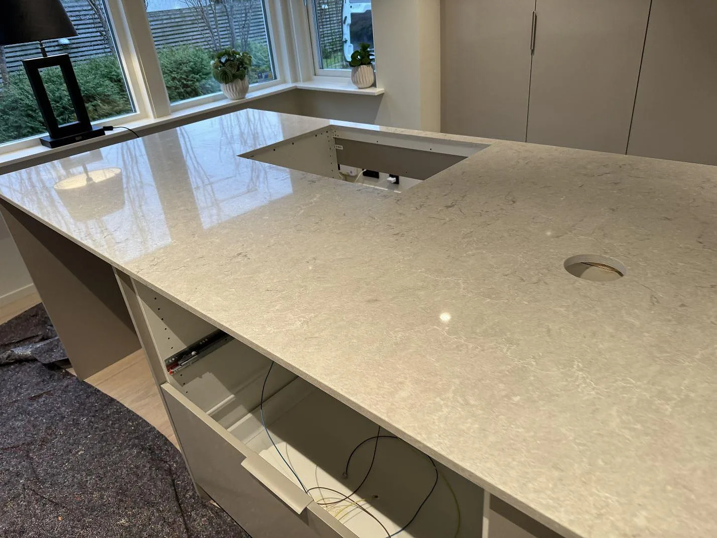 Närbild på polerad Caesarstone Bianco Drift köksbänkskiva med hällöppning och ljus ådring vid fönster i Halmstad.