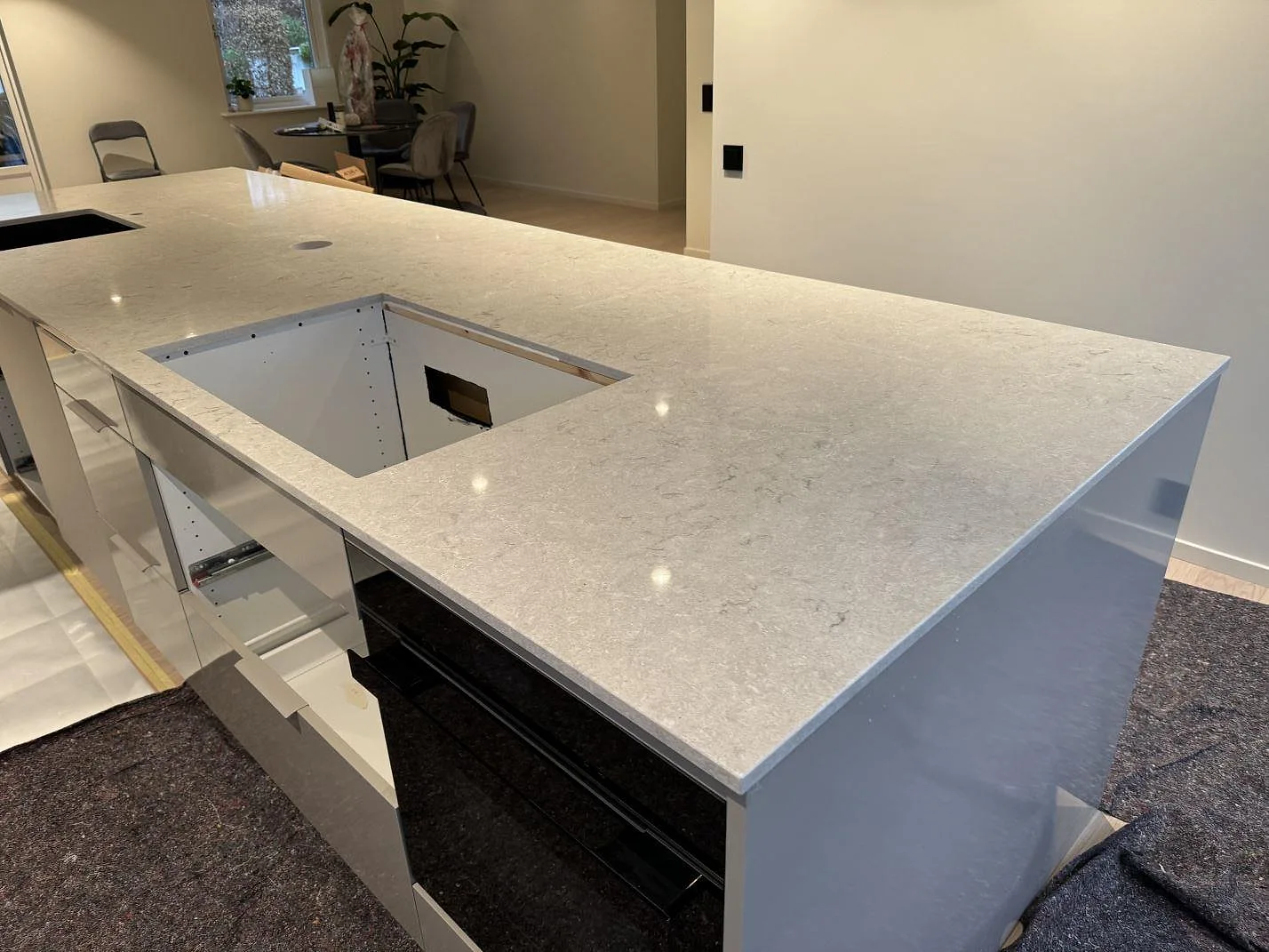Bred köksbänkskiva i 20 mm polerad Caesarstone Bianco Drift med stor hällöppning och öppen stomme under montering i Halmstad.
