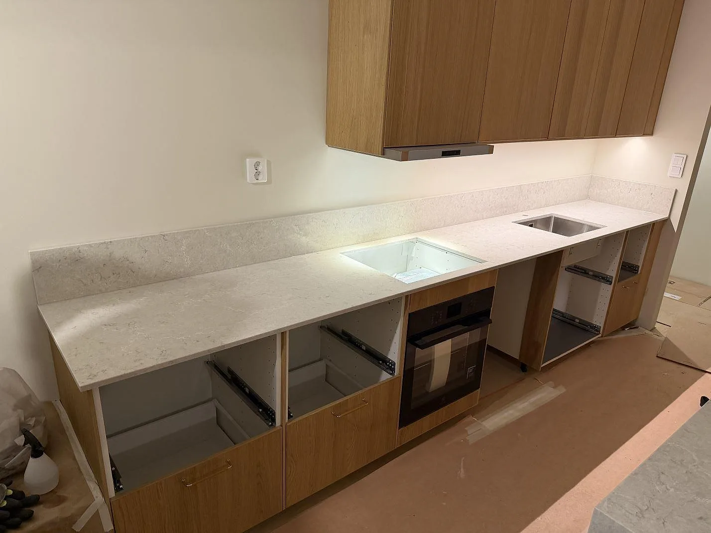 Köksbänkskiva i vit Caesarstone Bianco Drift, polerad kvartskomposit med grå ådring, med underlimmad rostfri diskho och uppvikt stänkkant i ett parallellkök i Karlstad.