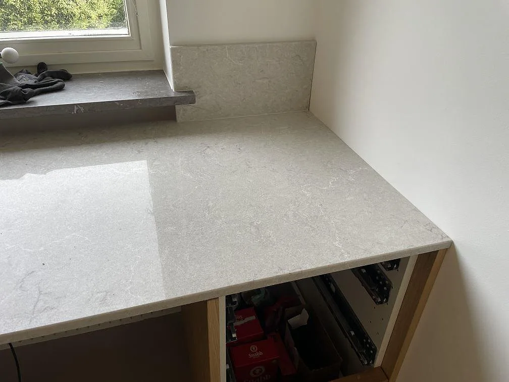 Sidodel av kök med polerad Caesarstone Bianco Drift bänkskiva, uppvikt stänkkant och ljus komposityta i Malmö.