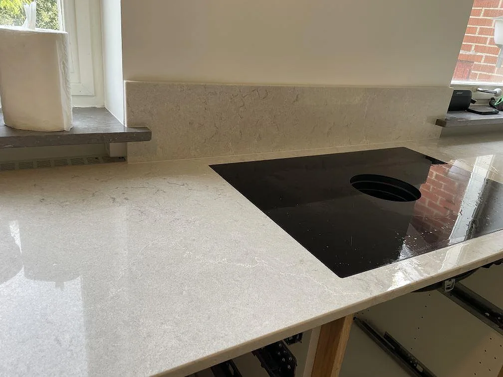 Närbild av svart induktionshäll i polerad köksbänkskiva i Caesarstone Bianco Drift med ljus komposityta i Malmö.