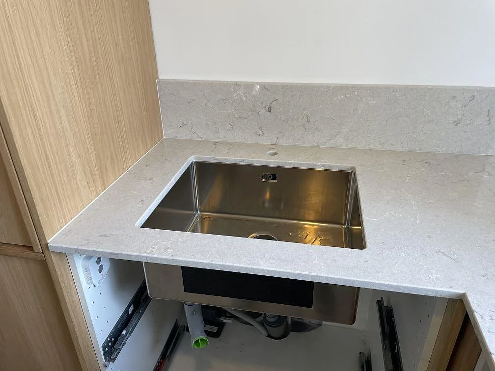 Underlimmad rostfri diskho i en polerad Caesarstone Bianco Drift bänkskiva med ljus ådring och stänkkant i Malmö.