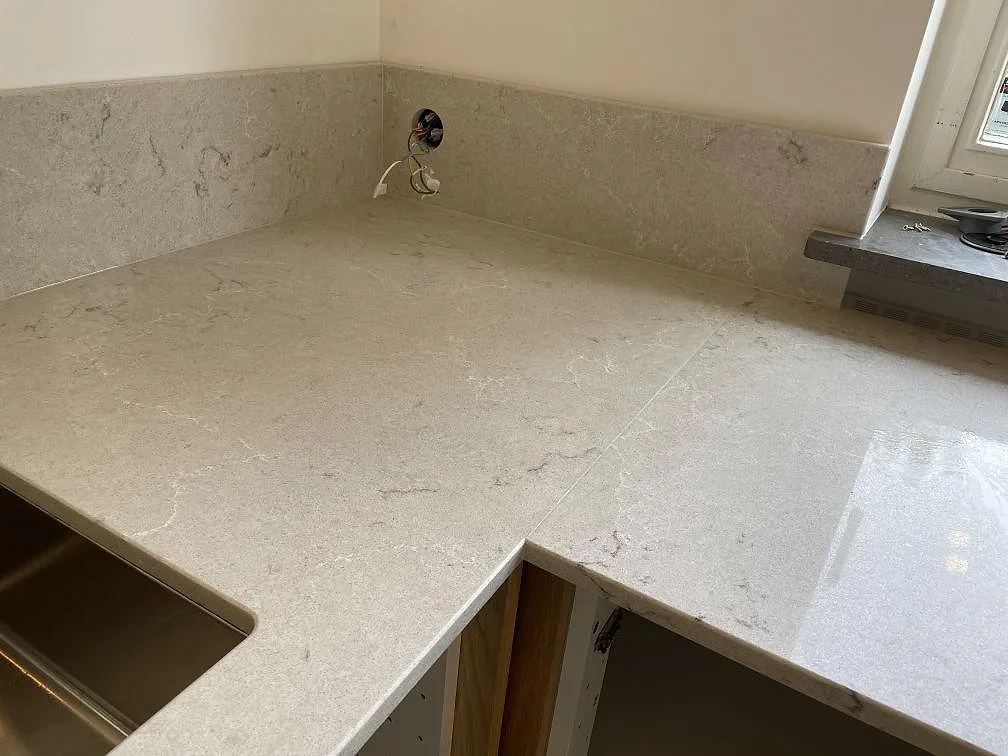 Hörndel av U-kök med polerad Caesarstone Bianco Drift bänkskiva, underlimmad rostfri diskho och uppvikt stänkkant i Malmö.