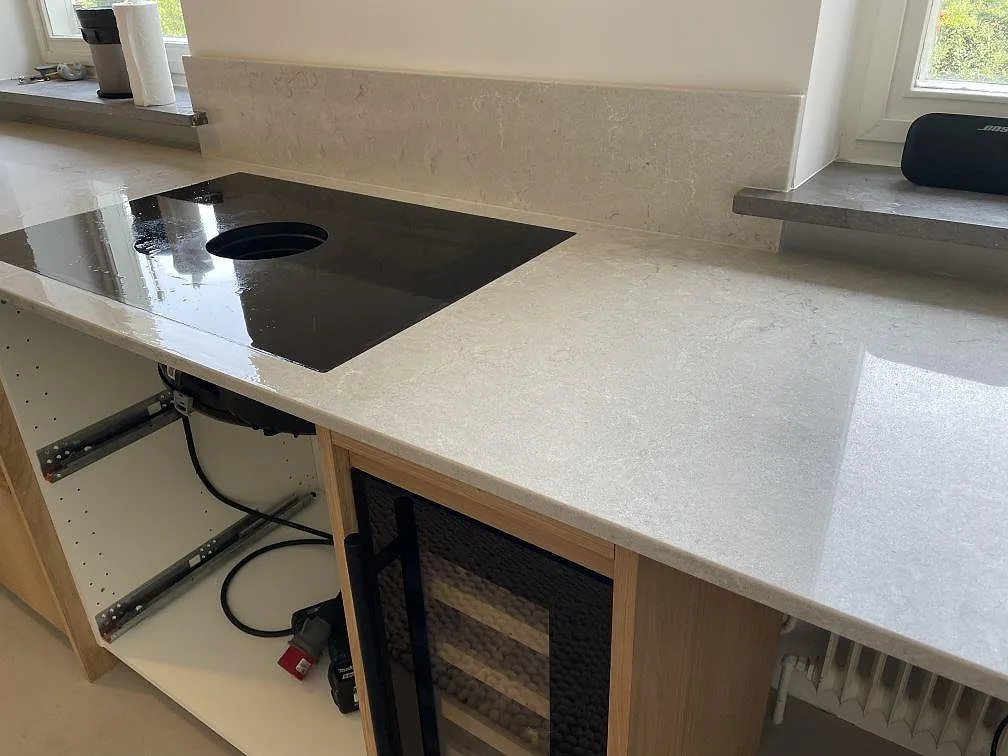 Polerad köksbänkskiva i Caesarstone Bianco Drift med svart induktionshäll, stänkkant och integrerad vinkyl i ett kök i Malmö.