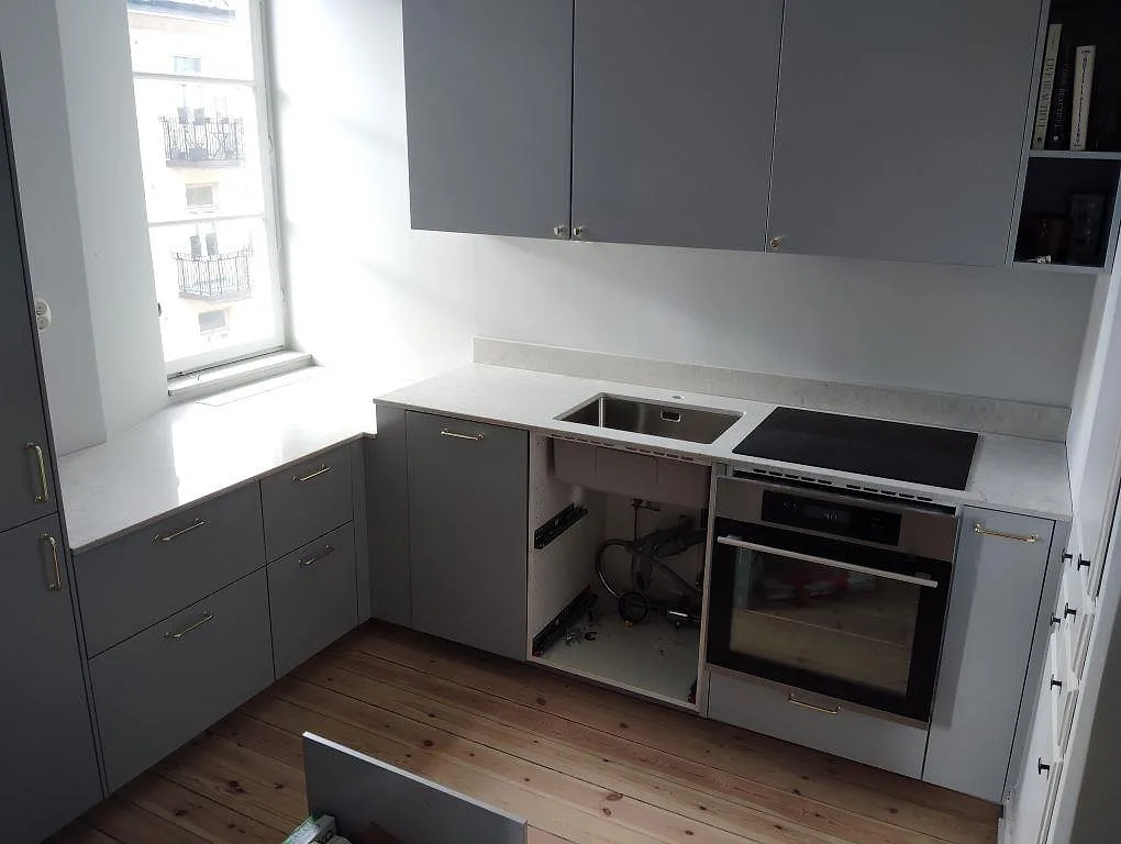 Köksbänkskiva i Caesarstone Bianco Drift, polerad komposit, med underlimmad rostfri diskho och svart häll vid fönster i Stockholm.