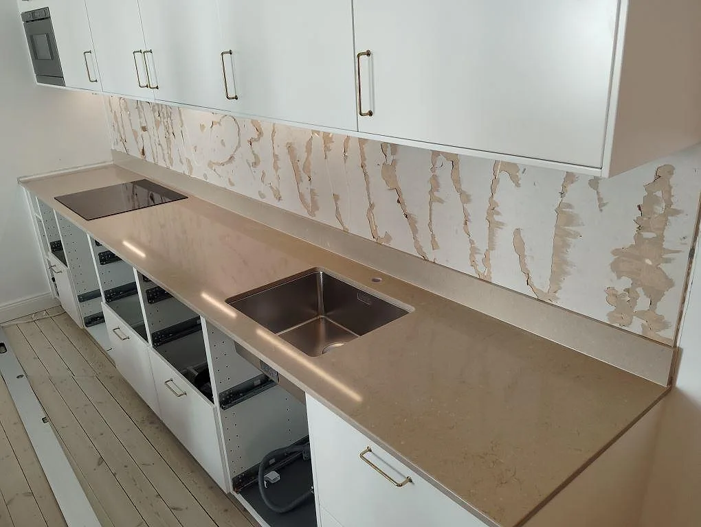 Köksbänkskiva i Caesarstone Bianco Drift, polerad komposit, med underlimmad rostfri diskho, svart häll och grenmönstrat stänkskydd i Stockholm.