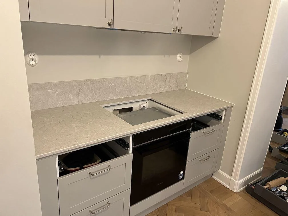 Polerad Caesarstone Bianco Drift som köksbänk i Stockholm, med stänkkant och öppen urtagning vid spiszonen under montering.