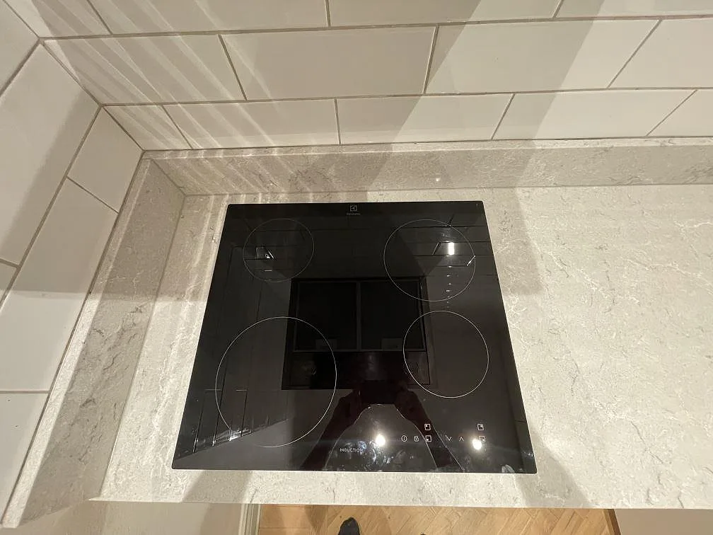 Infälld induktionshäll från Electrolux i polerad Caesarstone Bianco Drift bänkskiva, vit kvartskomposit med grå ådring, i ett kök i Stockholm.