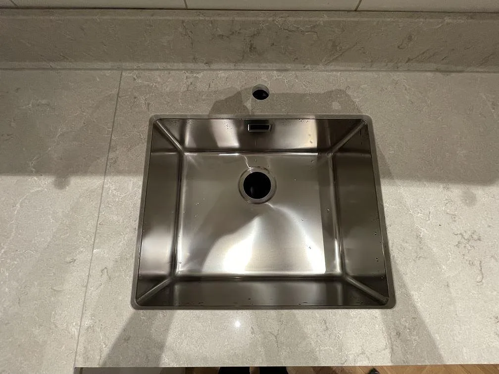 Underlimmad fyrkantig rostfri diskho i polerad Caesarstone Bianco Drift bänkskiva, vit kvartskomposit med grå ådring, i ett kök i Stockholm.