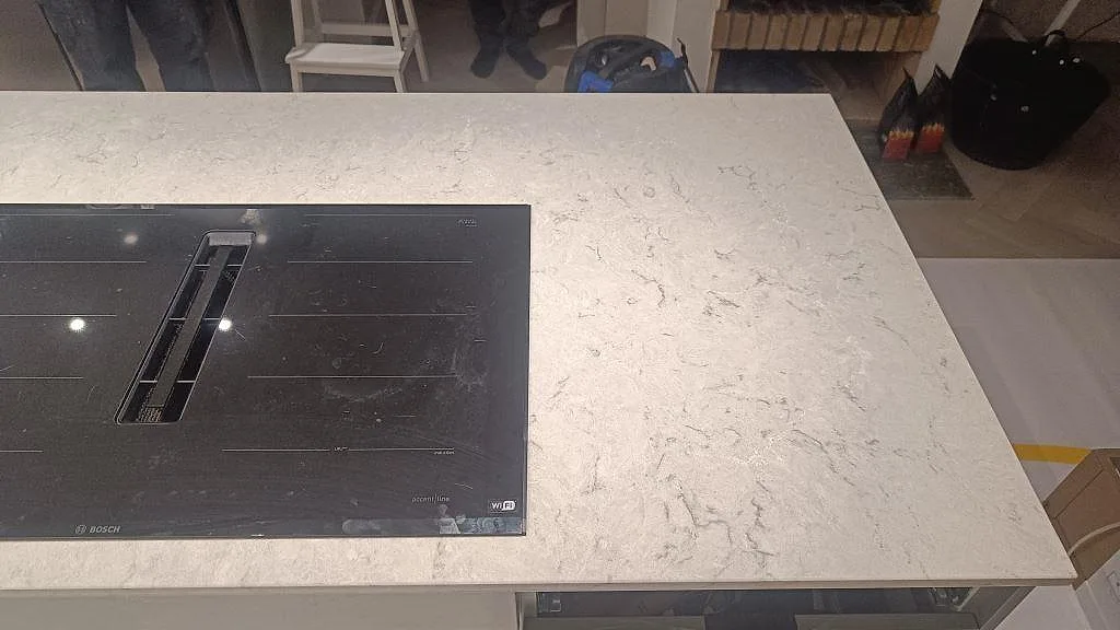 Polerad Caesarstone Bianco Drift på köksö med ljus ådring och induktionshäll i Tidaholm.