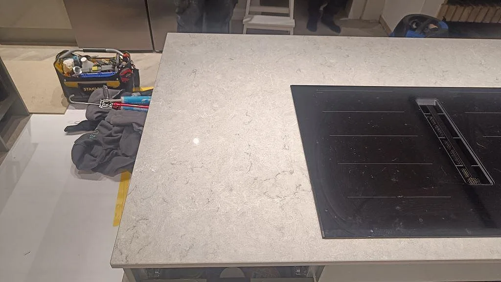 Detalj av polerad Caesarstone Bianco Drift runt induktionshäll på köksö under montering i Tidaholm.