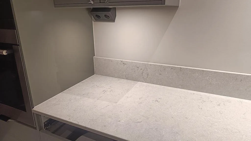 Bänkskiva i polerad Caesarstone Bianco Drift med matchande stänkkant vid grå köksskåp i Tidaholm.
