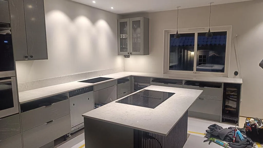 Köksbänkskiva och köksö i polerad Caesarstone Bianco Drift med induktionshäll i ett grått kök i Tidaholm.
