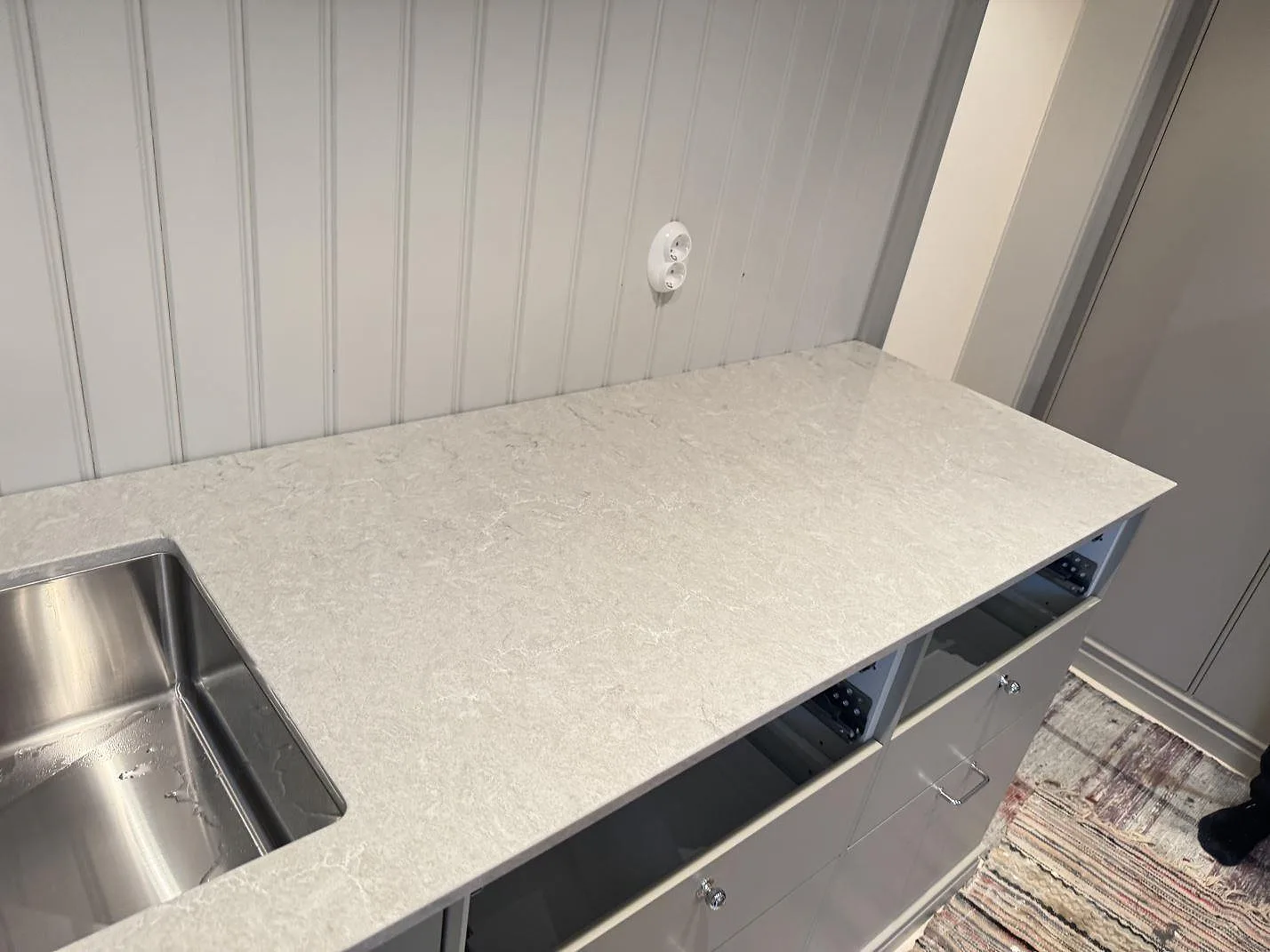 Väggmonterad köksbänk i polerad Caesarstone Bianco Drift med diskho och pärlspont bakom i Vårgårda.