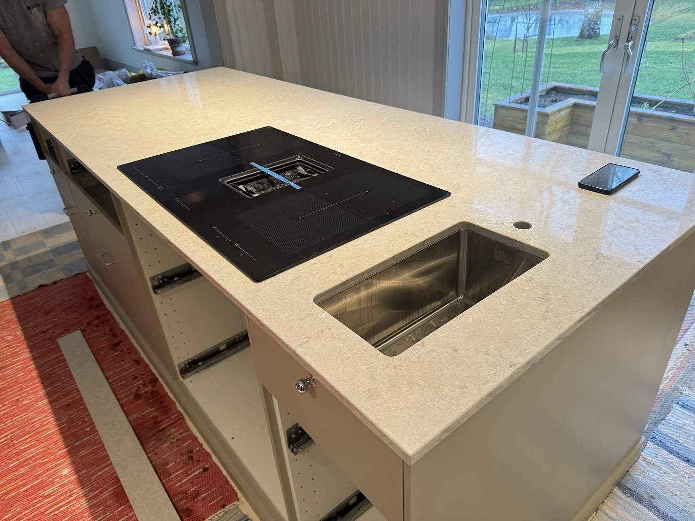 Polerad köksö i Caesarstone Bianco Drift med rostfri diskho och svart häll under montering i Vårgårda.