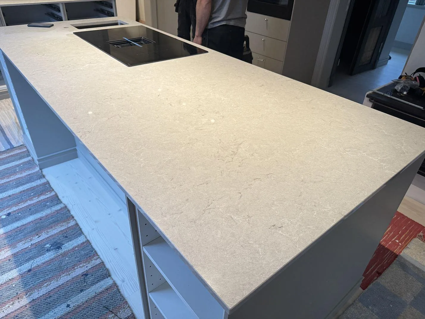 Lång köksö i Caesarstone Bianco Drift, polerad komposit med häll och ljus ådring i ett kök i Vårgårda.