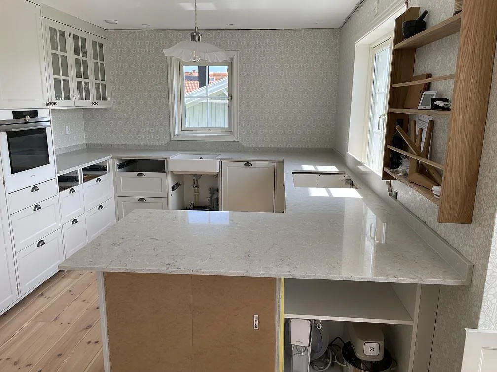 Köksbänkskiva i Caesarstone Bianco Drift, polerad kvartskomposit, med bred arbetsyta och stänkkant i ett kök i Värmdö.