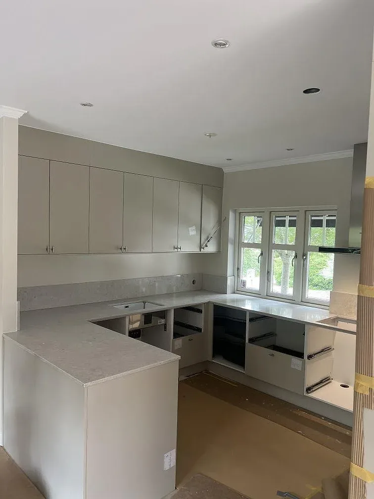 Köksbänkskiva i polerad Caesarstone Bianco Drift med stänkskydd, hällöppning och diskho i ett kök under montering i Varberg.