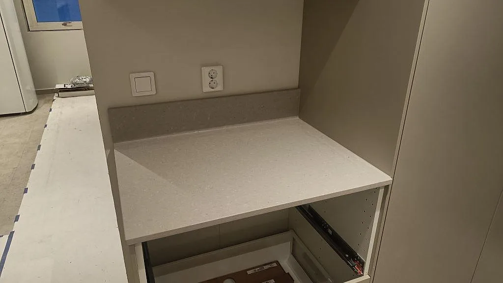 Sidobänk i matt Caesarstone Clamshell med låg stänkkant vid högskåp i kök i Åseda.