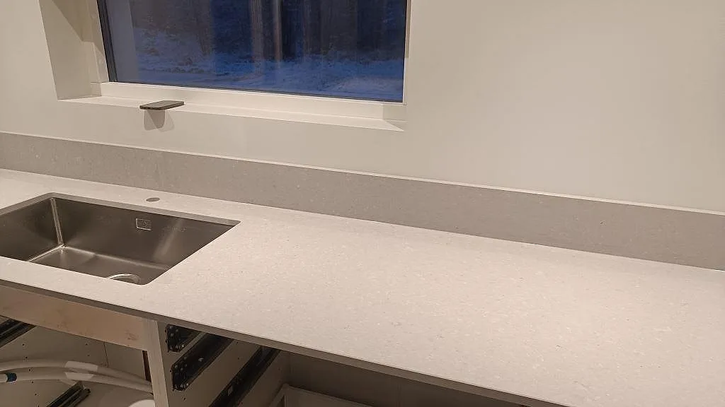 Väggbänk i matt Caesarstone Clamshell med rostfri diskho och stänkkant under fönster i Åseda.
