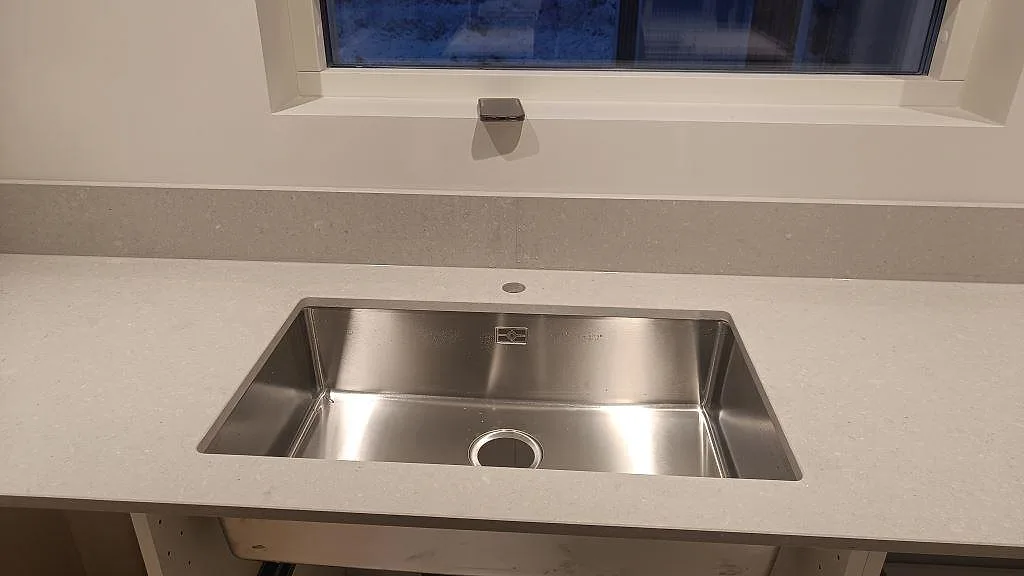 Närbild av rostfri diskho i matt Caesarstone Clamshell med stänkkant vid fönster i Åseda.
