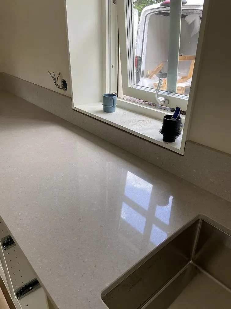 Köksbänkskiva i Caesarstone Clamshell, polerad beige kvartskomposit, med underlimmad rostfri diskho vid fönstret i ett kök i Emmaboda.