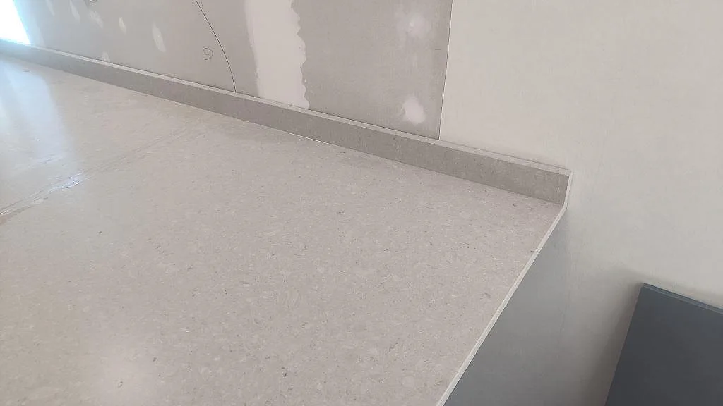 Installerad Caesarstone Clamshell bänkskiva i matt kvartskomposit med låg stänkkant längs väggen i Falköping.