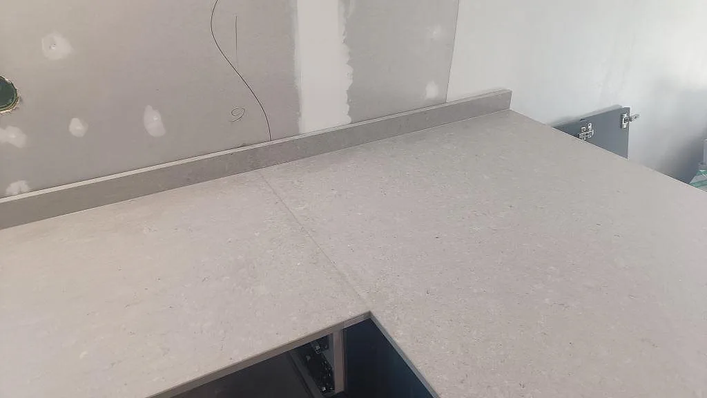 Detalj av matt Caesarstone Clamshell bänkskiva med uppvikt stänkkant och ljus stenstruktur i Falköping.