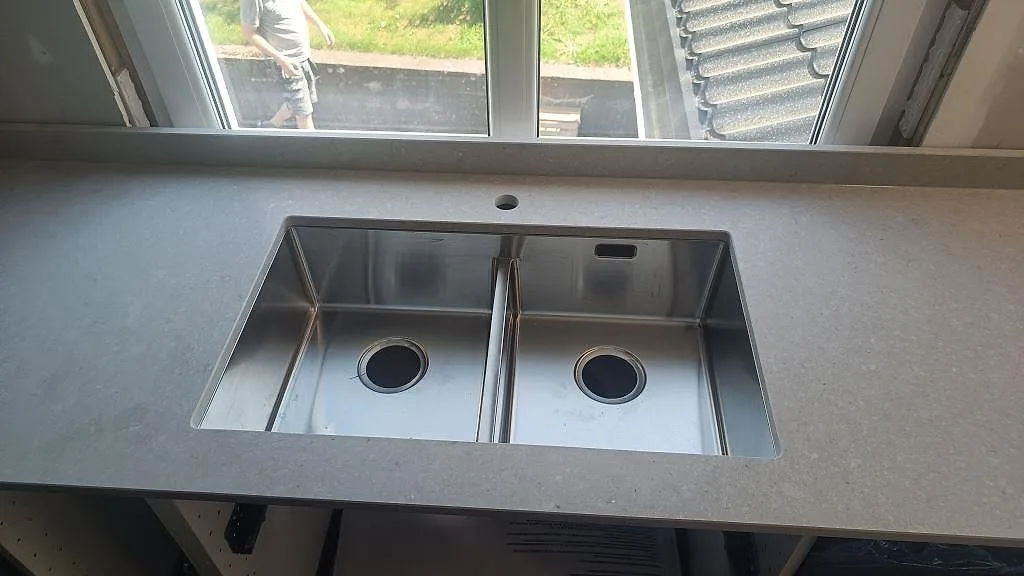 Underlimmad dubbelho i rostfritt stål monterad i matt Caesarstone Clamshell bänkskiva vid fönster i Falköping.