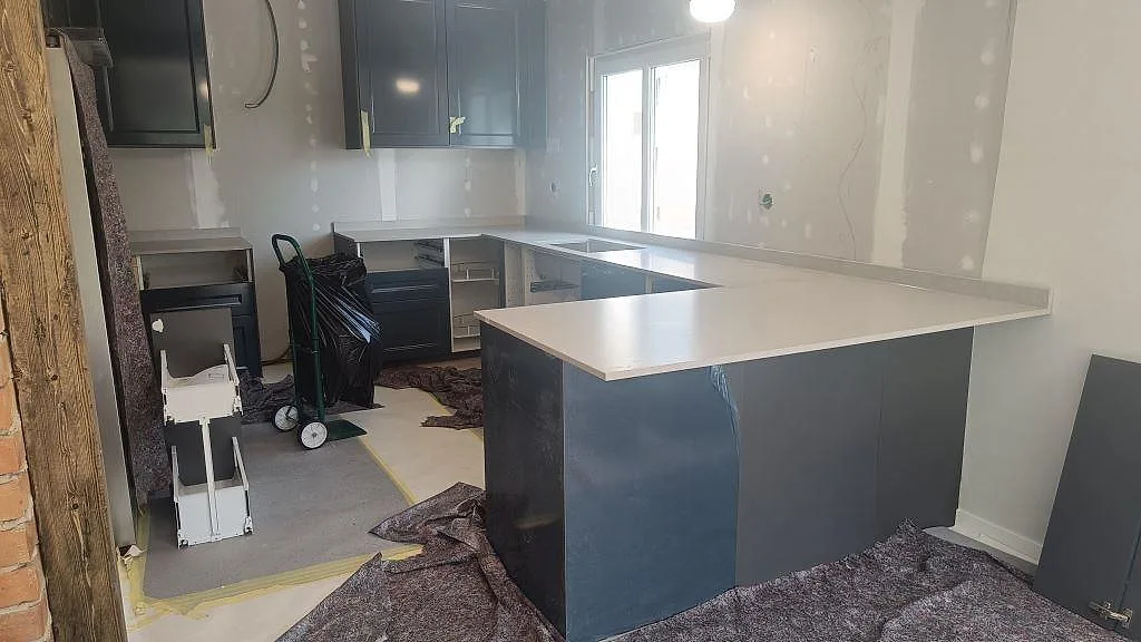 Köksbänkskiva i matt Caesarstone Clamshell, kvartskomposit, i ett U-format kök med gråblå stommar i Falköping.
