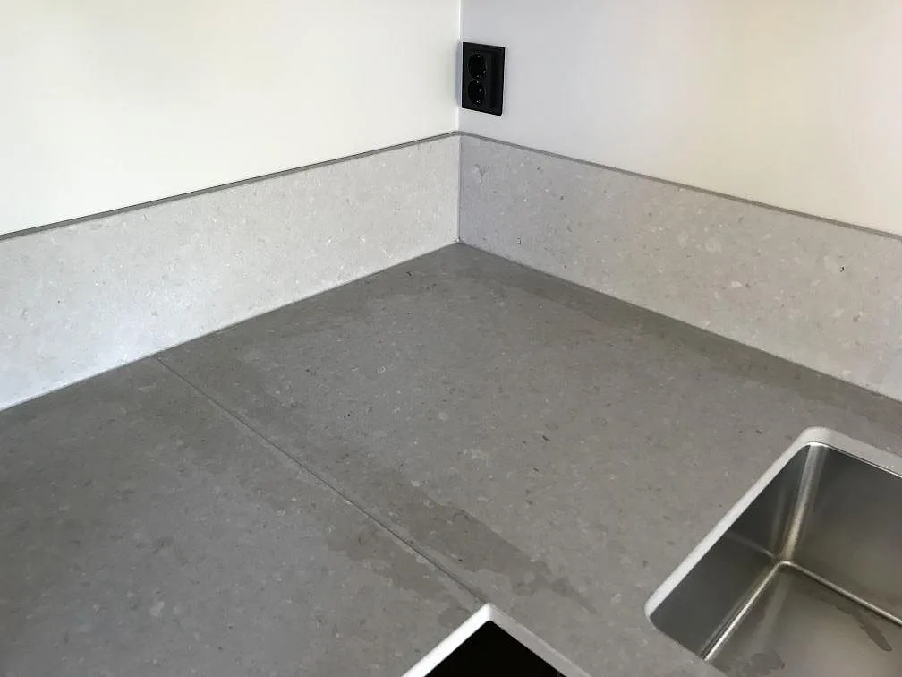 Hörnparti av köksbänkskiva i beige Caesarstone Clamshell med uppvikt stänkkant och kant av rostfri diskho i Göteborg.