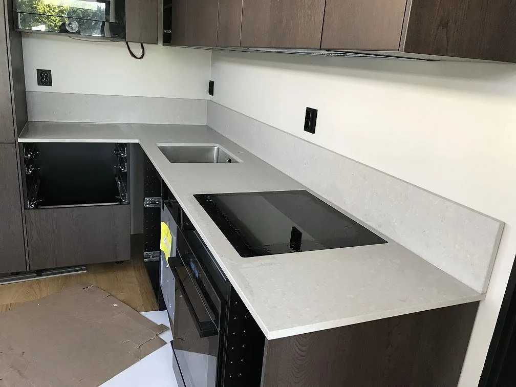 Köksbänkskiva i Caesarstone Clamshell, beige matt kvartskomposit, i ett L-format kök med underlimmad rostfri diskho och infälld induktionshäll i Göteborg.