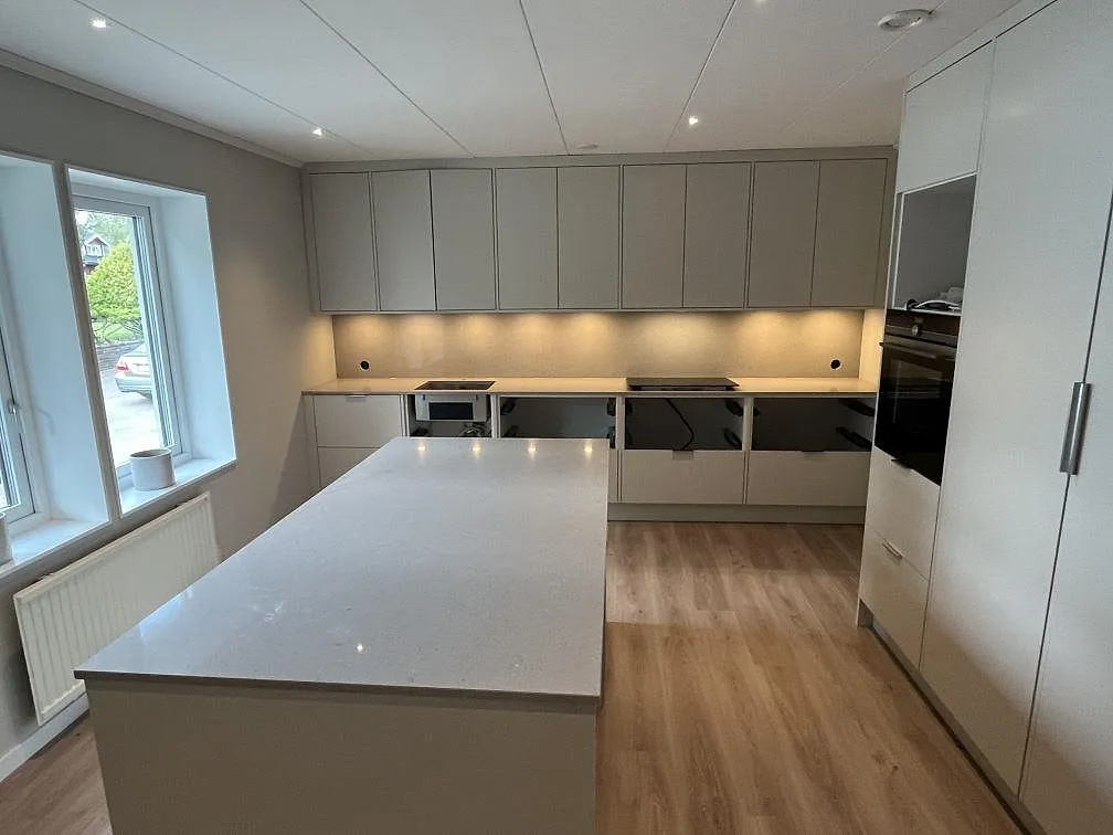 Köksbänkskiva och köksö i beige Caesarstone Clamshell komposit, polerad, i ett ljust kök under montering i Halmstad.
