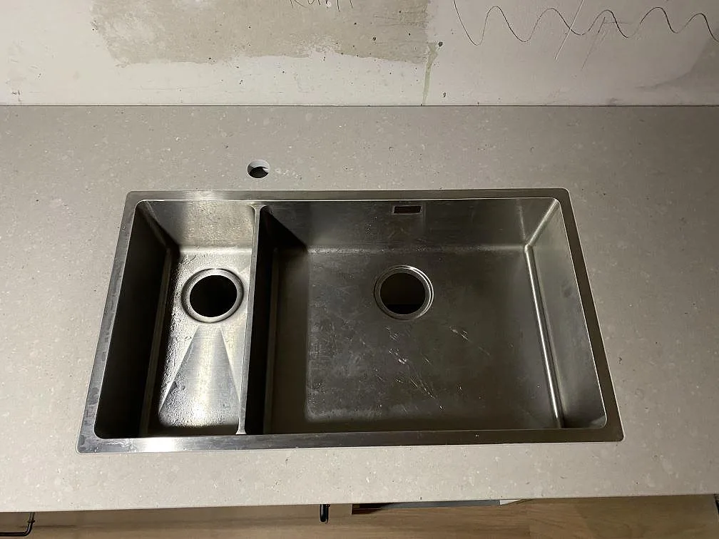 Detalj av synlig rostfri diskho i köksbänkskiva av matt Caesarstone Clamshell i Lerum.