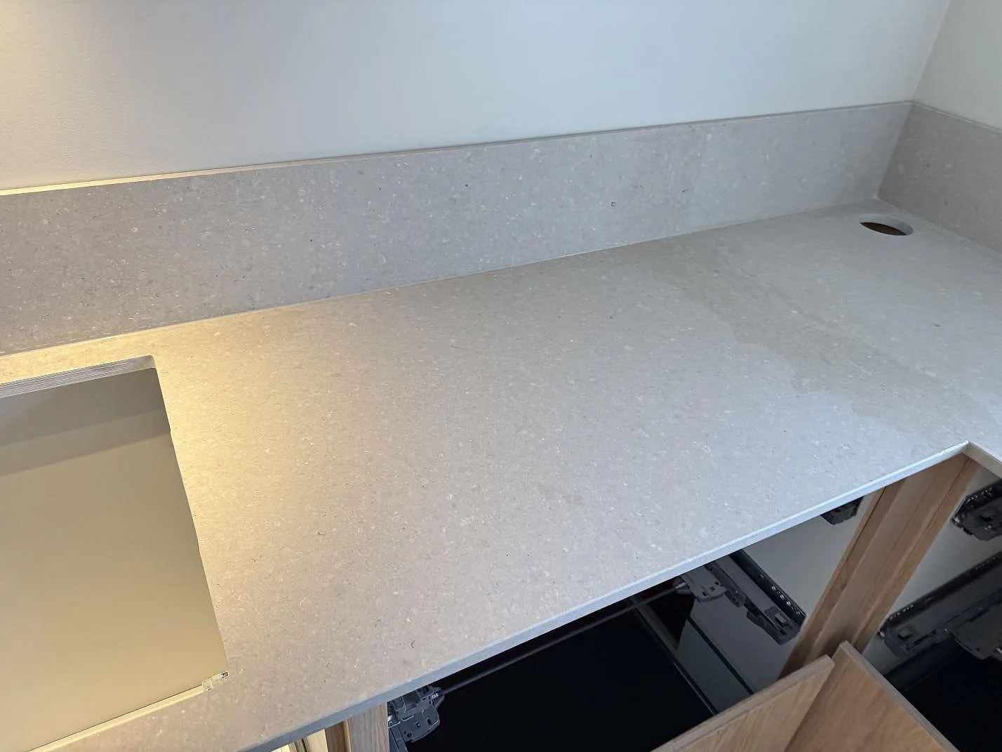 Bänkskiva i matt Caesarstone Clamshell komposit med stänkkant, rektangulär ursågning och runt armaturhål i ett badrum i Löddeköpinge.