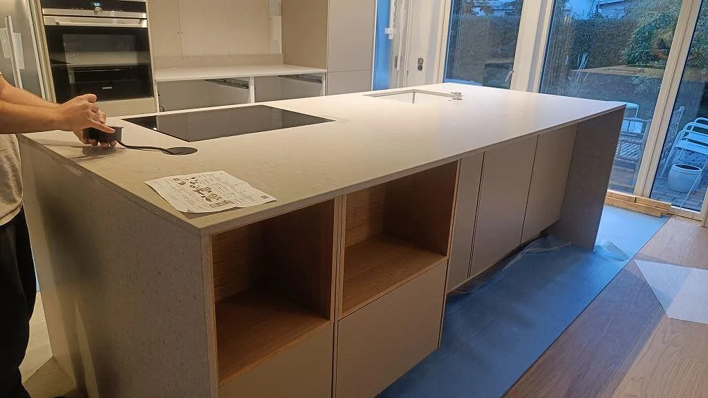 Köksbänkskiva och köksö i Caesarstone Clamshell, matt beige kvartskomposit, med nedsänkt induktionshäll i ett kök i Lomma.