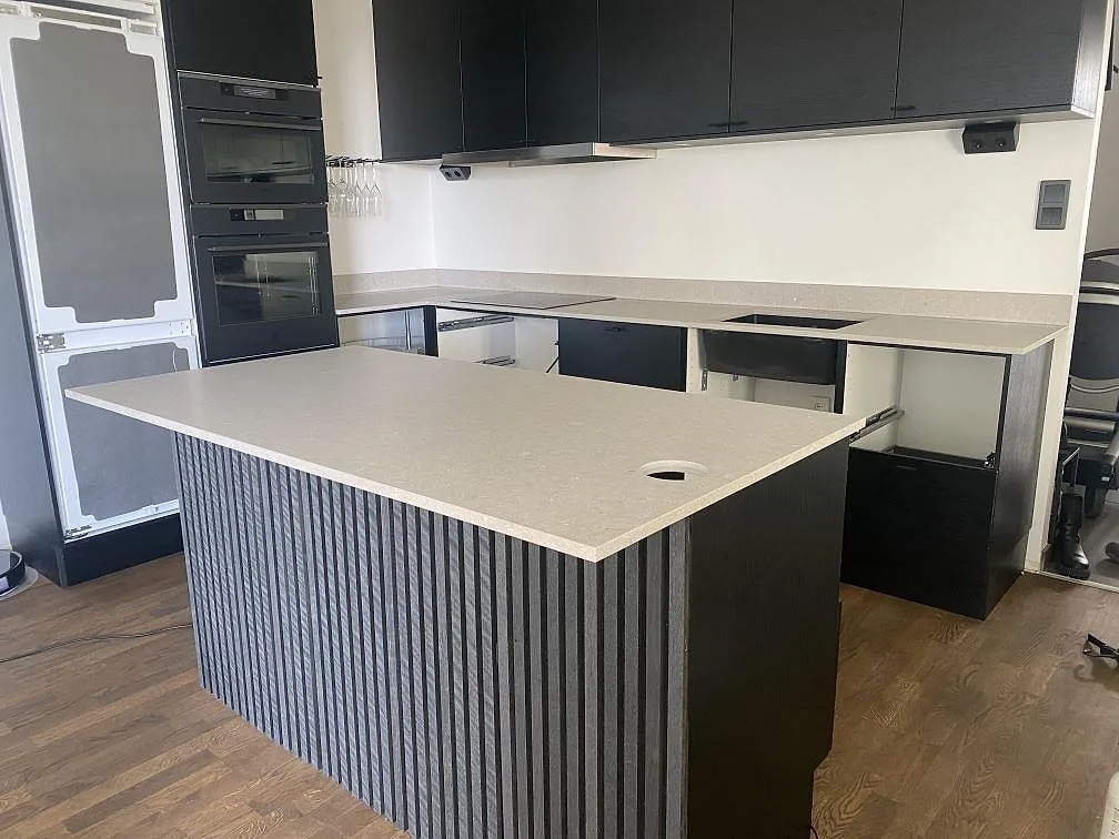Köksbänkskiva i krämvit Caesarstone Clamshell, matt kvartskomposit, i ett U-format kök med köksö och mörka skåp i Malmö.