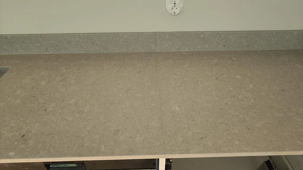 Rak köksbänk i Caesarstone Clamshell, polerad ljusgrå komposit med stänkkant under montering i Malmö.