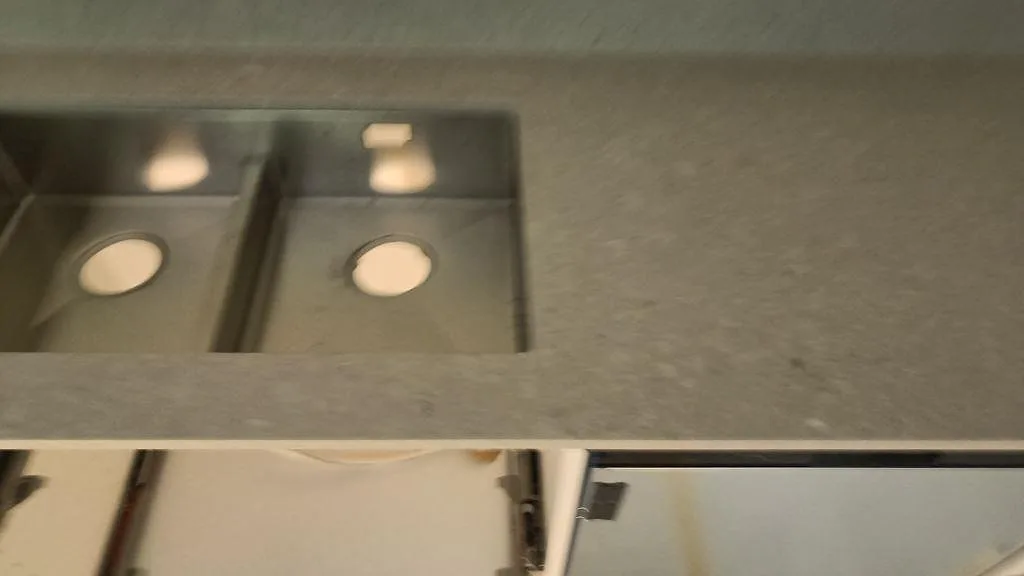 Detalj av underlimmad dubbel diskho i rostfritt stål mot ljusgrå Caesarstone Clamshell komposit i Malmö.