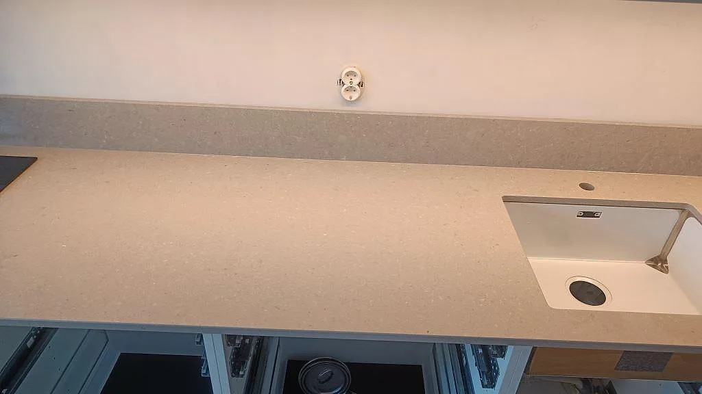 Lång arbetsyta i polerad Caesarstone Clamshell med rostfri diskho och synlig hällzon under montering i Malmö.