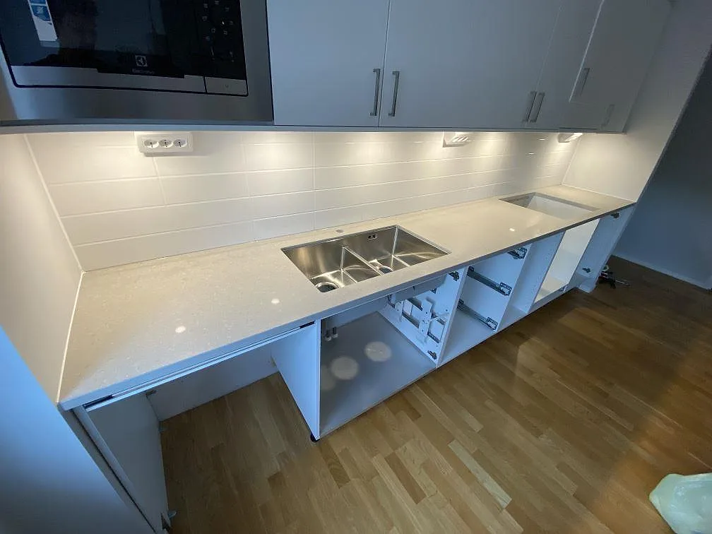 Köksbänkskiva i polerad Caesarstone Clamshell, ljus kvartskomposit, med underlimmad rostfri dubbelho och hällurtag i ett kök i Malmö.