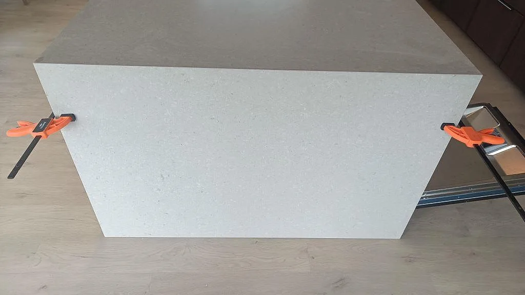 Frontvy av köksö i Caesarstone Clamshell med nedgående gavel, tvingar och matt ljusgrå stenyta i Nättraby.