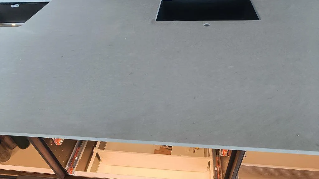 Närbild på matt Caesarstone Clamshell i ljusgrå kvartskomposit med urtag och synlig stenskiva över öppna köksstommar i Nättraby.